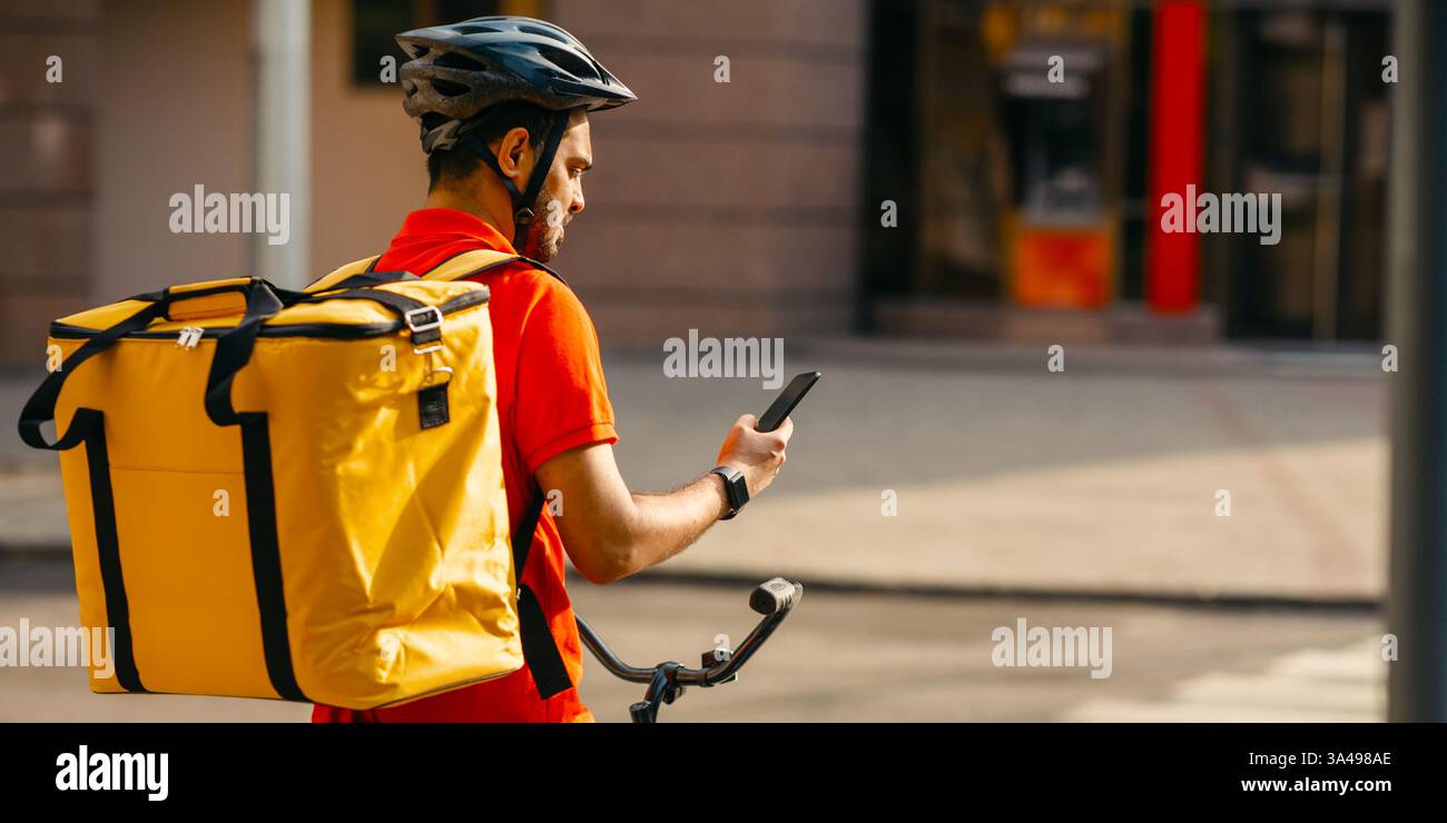 Junge männliche Radfahrer mit Kurier Liefertasche mit Handy auf der Straße, um Adresse des Kunden in der mobilen Anwendung zu suchen Stockfoto