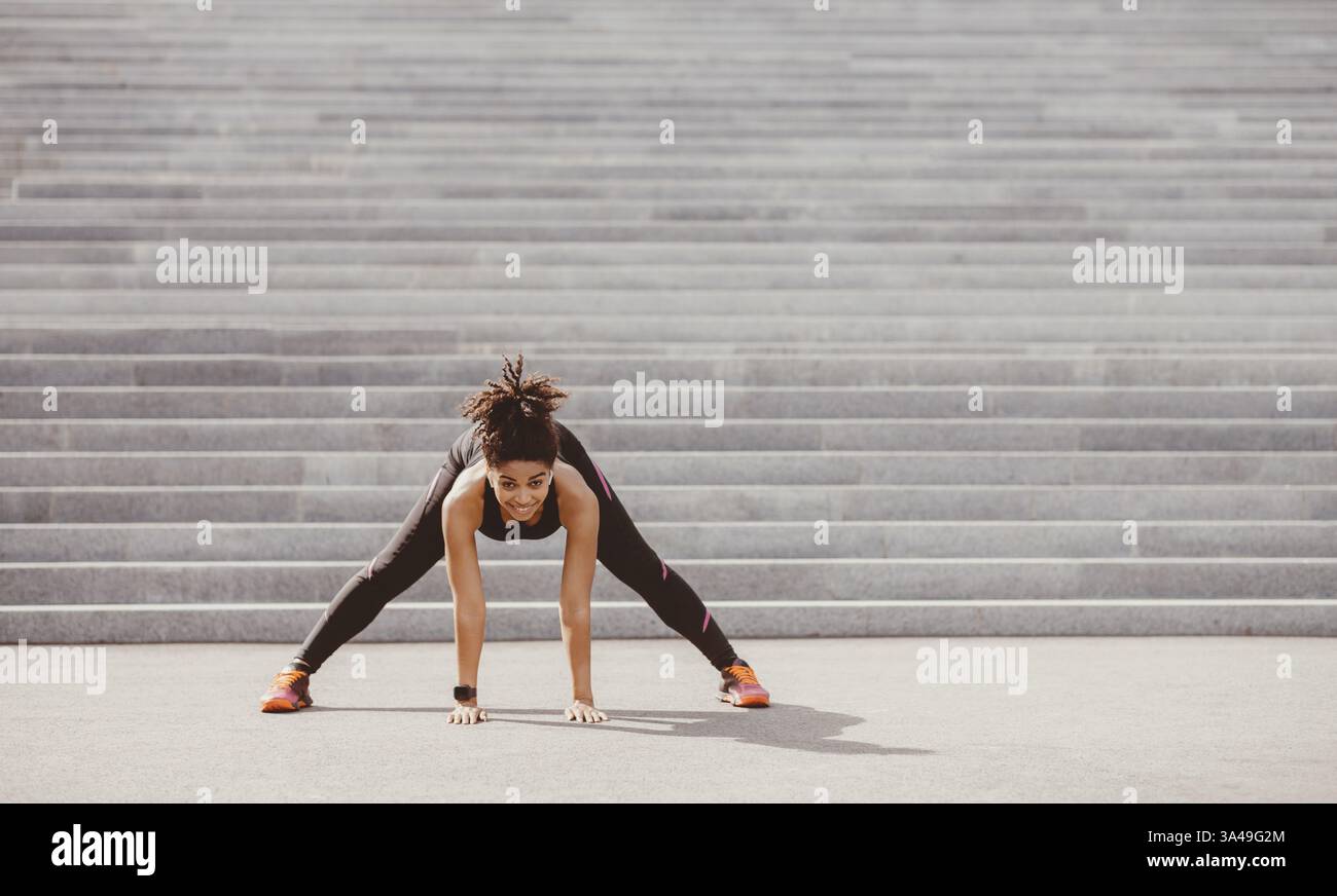 Übungen für Flexibilität. Fröhliche afroamerikanische Mädchen in Sportswear mit Fitness-Tracker tun Stretching Stockfoto