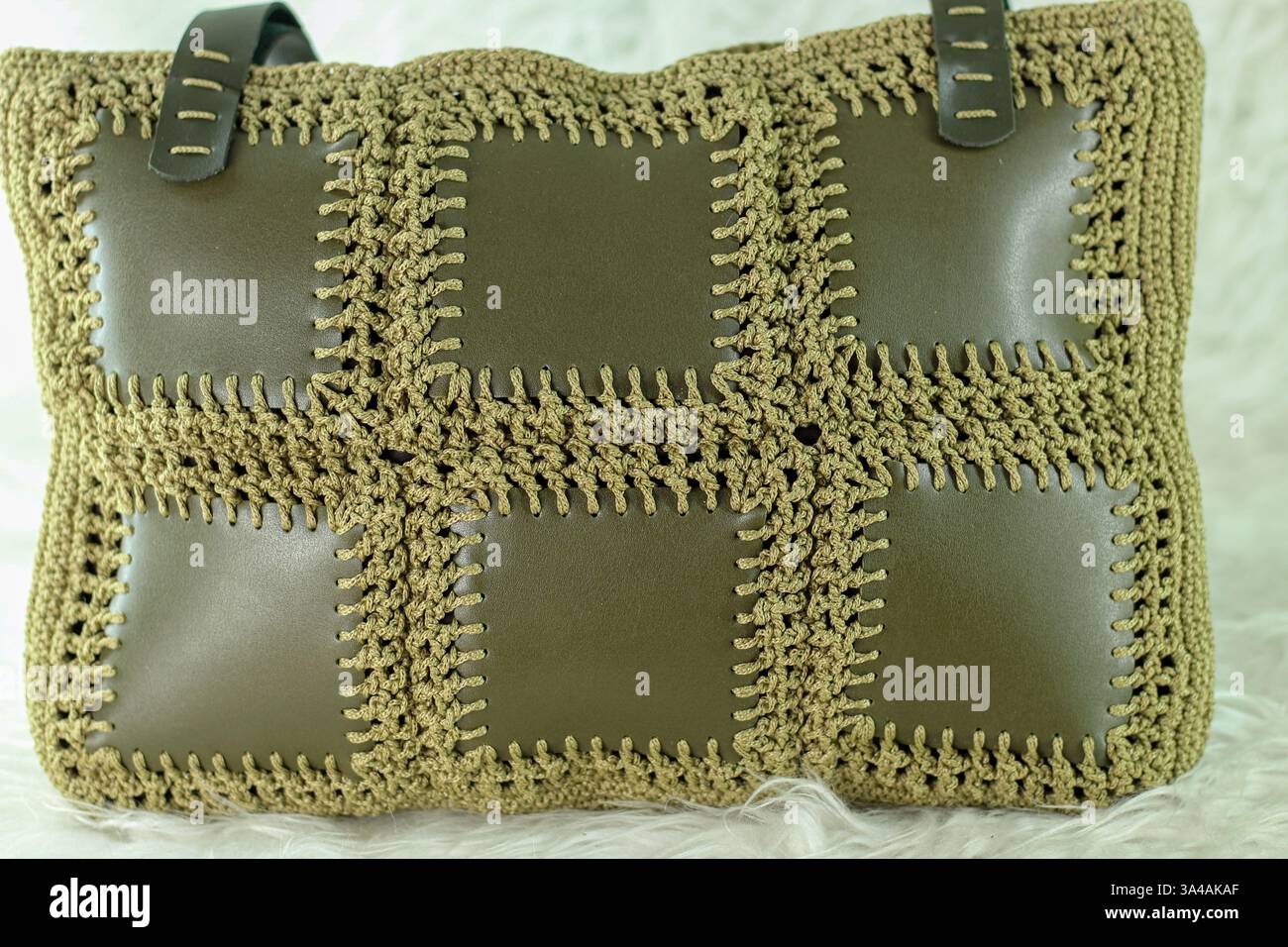 Grüne Schultertasche aus Kunstlederstücken auf einer weißen flauschigen Decke gestrickt. Nahaufnahme. Stockfoto