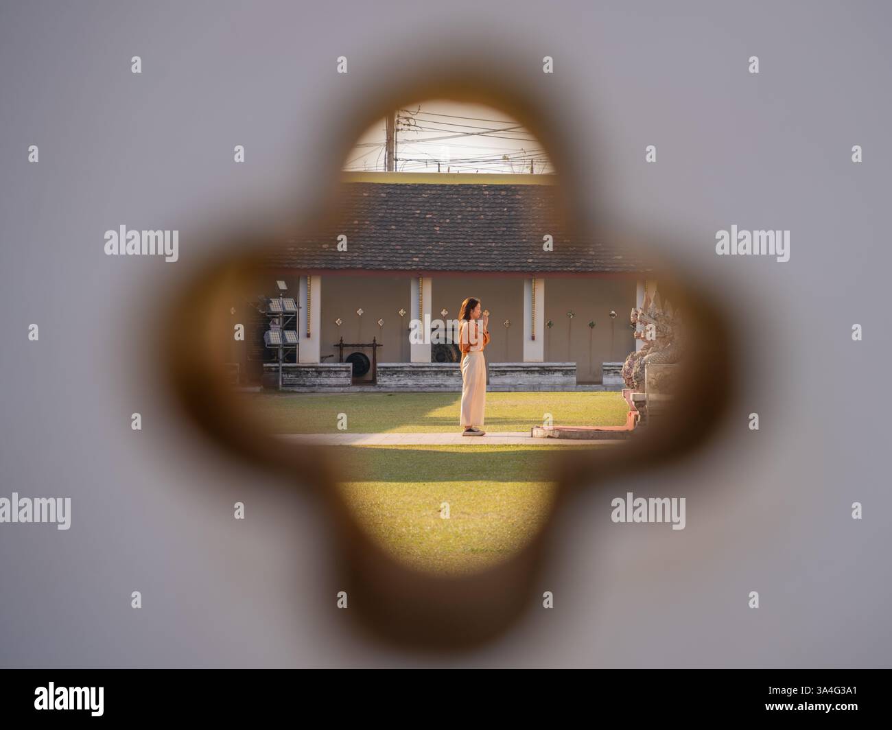 Eine Frau, die durch eine Schlüssellochöffnung gerahmt wurde, blickte auf einen Tempelhof in Laos und hielt einen Moment der Ruhe und kulturellen Entdeckungen fest Stockfoto