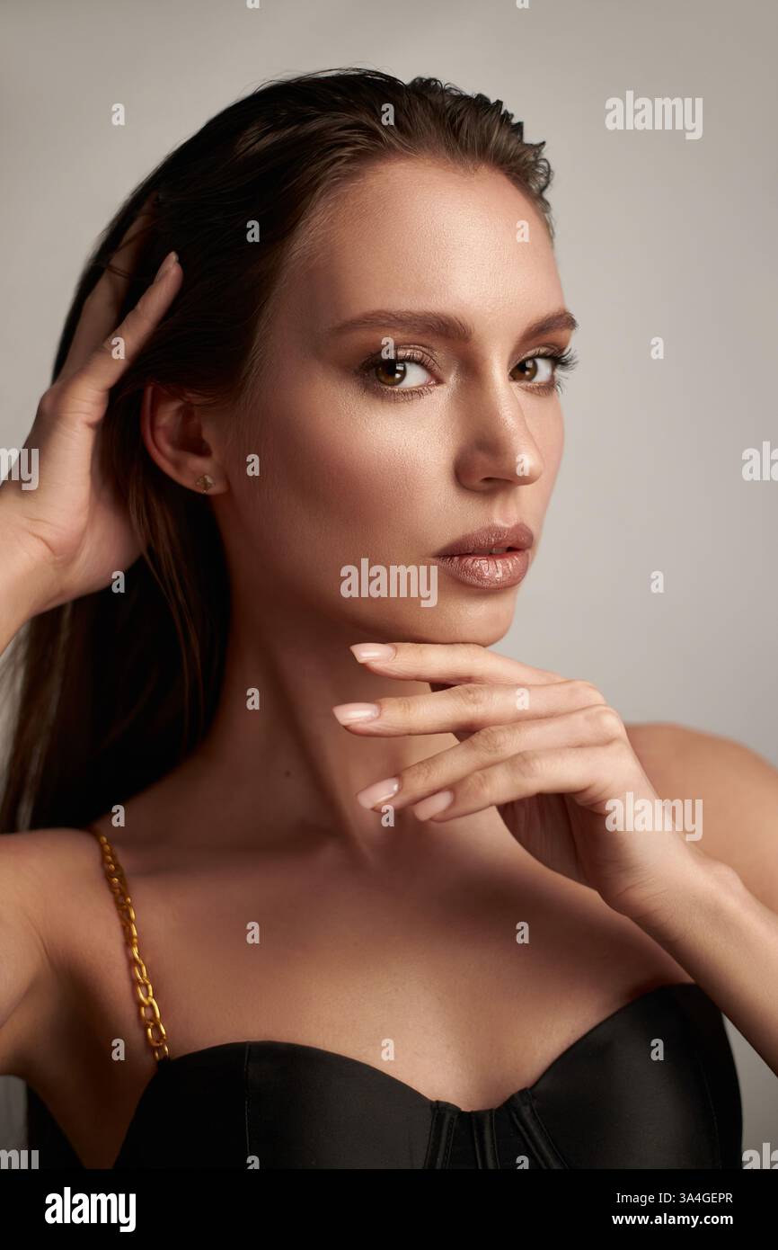 Das Model mit langen Haaren zeigt sich selbstbewusst in einem stilvollen schwarzen Outfit. Mit den Händen wird das Gesicht umrahmt, während es ein Gefühl von Pose und Charme ausstrahlt Stockfoto