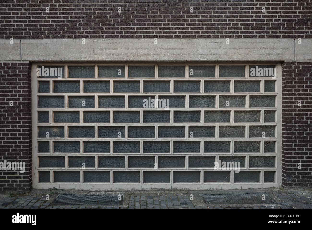 Eine symmetrische Glasmauerwand mit einem modernen geometrischen Muster, eingerahmt von dunkelbraunen Ziegeln und Betonelementen. Stockfoto