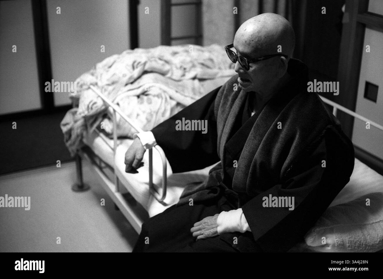 Februar 2003; Oshima Island, JAPAN; Herr Nambu, ein Patient, der auf Oshima Island Leprakolonie lebt, wacht jeden Morgen sehr früh auf, sitzt auf seinem Bett, während er darauf wartet, dass ein Arzt kommt, der ihm hilft, sich anzuziehen. Mr. Nambu, in seinen Achtzigern und blind, hat sein ganzes Leben auf Oshima Island verbracht. Aus Schande änderten die meisten Patienten ihren Namen, um Familie und Freunde nicht in Verlegenheit zu bringen. Sie brachen auch alle Verbindungen ab. Daher konnte oder wollte niemand sie beanspruchen, als sie starben. Als Aussätzige in ein Zentrum gezwungen wurden, wurden sie aus Angst vor anderen ansteckenden Krankheiten unter Quarantäne gestellt, ihre Kleidung und ihr Geld ausgezogen. Stockfoto