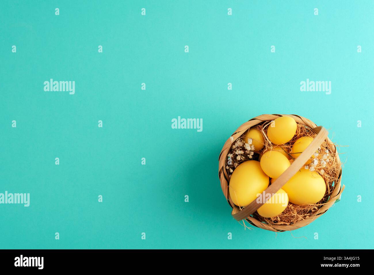 Korb mit gelben Ostereiern, Stroh und getrockneten Blumen auf pastellfarbenem türkisfarbenem Hintergrund. Draufsicht, flach, Kopierbereich Stockfoto