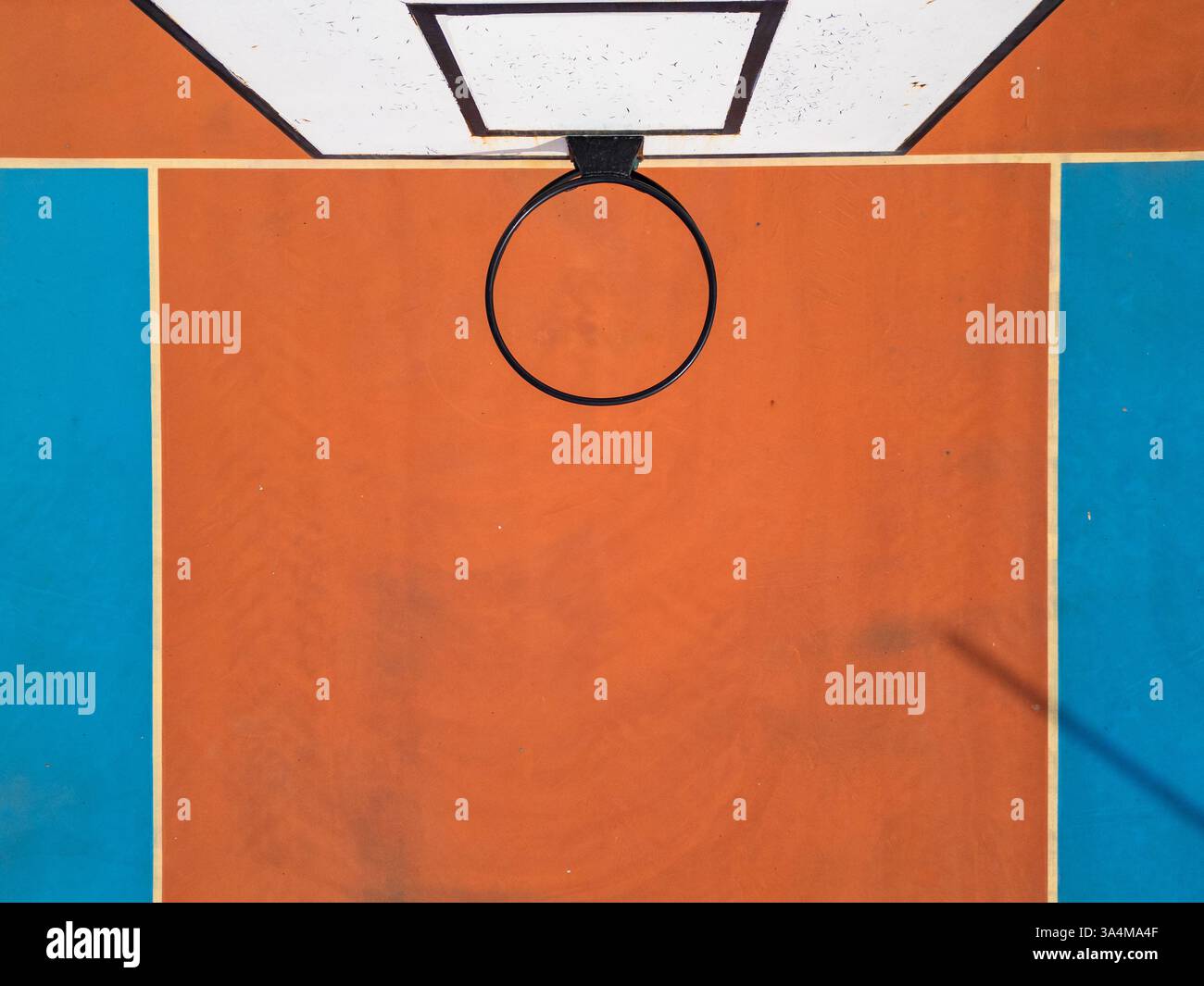 Aus der Vogelperspektive auf einen Basketballkorb und einen farbenfrohen Platz mit leuchtenden orangefarbenen und blauen Abschnitten. Das symmetrische Layout und die kräftigen Farben sorgen für eine beeindruckende Schärfe Stockfoto