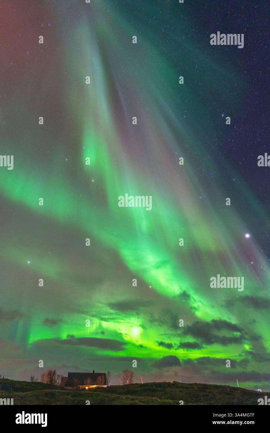 Wunderschöne Equinox Aurora Borealis über der Insel Hillesøya, tanzende Nordlichter mit klaren farbigen Lichtstrahlen, geschütztes Haus auf einem Hügel Stockfoto