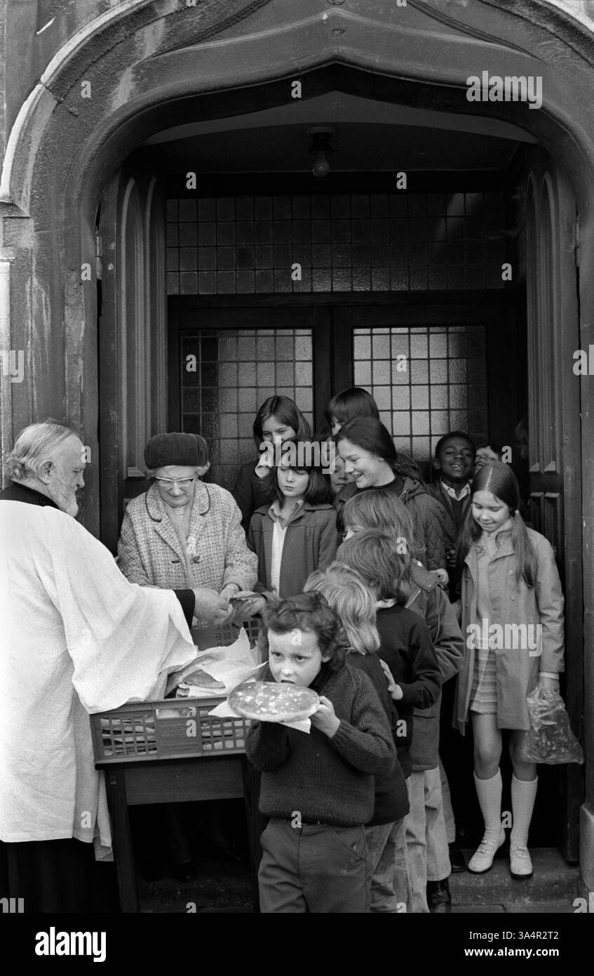 Tuppenny Starvers sind große Obstbrötchen, die jeden Osterdienstag verteilt werden. Der Reverend Jones vergibt 80 Tuppenny Starvers an Kinder und Einheimische, die an der jährlichen christlichen Feier in St. Michael on the Mount Without Church, St. Michaels Hill, Bristol, teilnehmen. Die Praxis wurde aus einem 1739 hinterlassenen Nachlass finanziert. England 1974 1970er Jahre UK HOMER SYKES. Stockfoto
