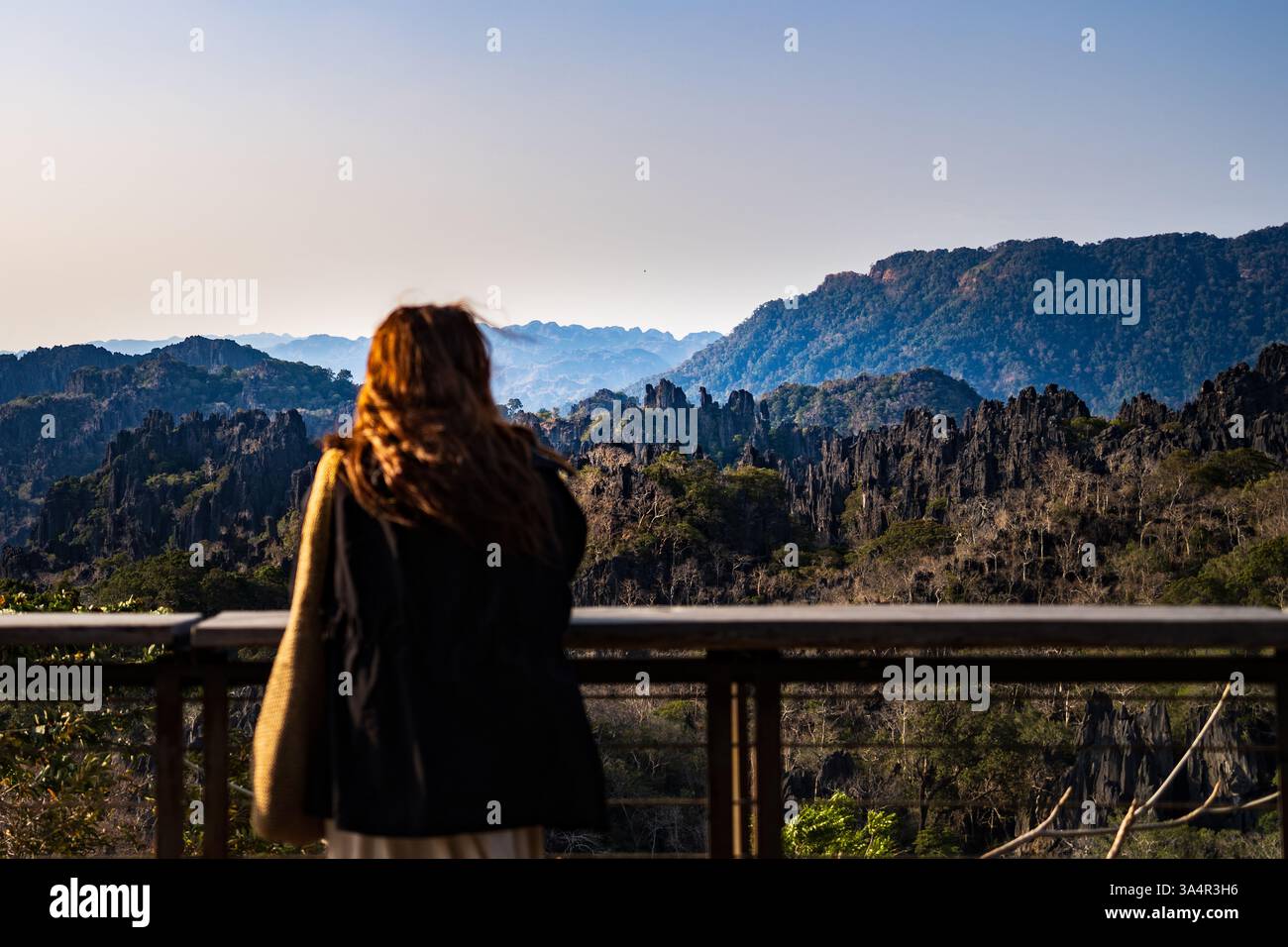 Frau, die auf einem Aussichtspunkt in den Bergen steht, Arme weit offen und das weite Tal und die zerklüfteten Gipfel in Südostasien bewundert. Stockfoto