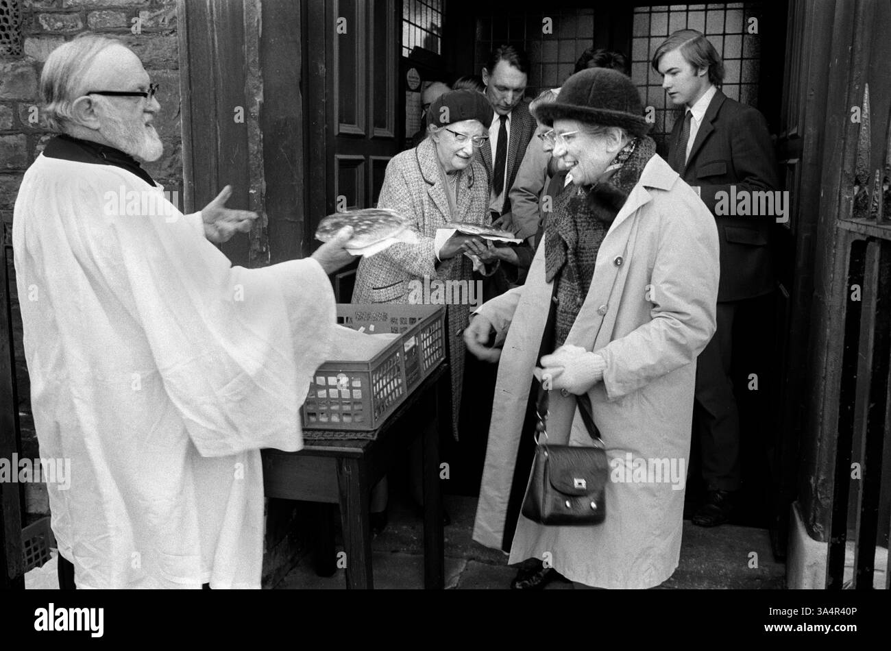 Ostern Großbritannien Erbe. Tuppenny Starvers sind große Obstbrötchen, die jeden Osterdienstag verteilt werden. Der Reverend Jones vergibt 80 Tuppenny Starvers an Kinder und Einheimische, die an der jährlichen christlichen Feier in St. Michael on the Mount Without Church, St Michaels Hill, Bristol teilnehmen. Die Praxis wurde aus einem Vermächtnis finanziert, das 1739 für sie hinterlassen wurde. England 1974 1970er Jahre UK HOMER SYKES. Stockfoto