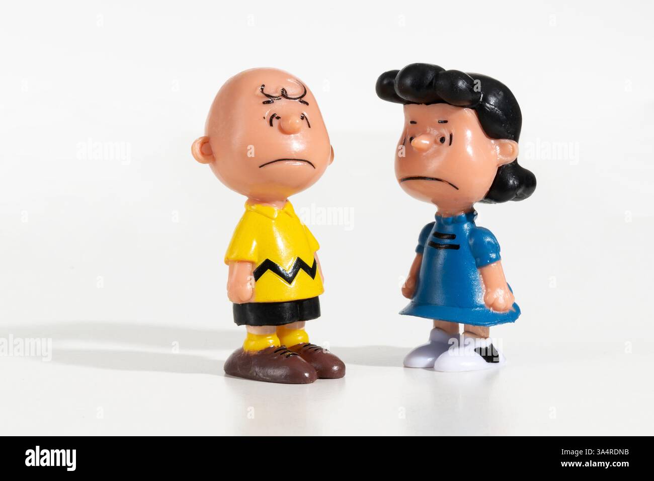 Figuren von Charlie Brown und Lucy van Pelt stehen zusammen mit traurigem Ausdruck auf weißem Hintergrund Stockfoto