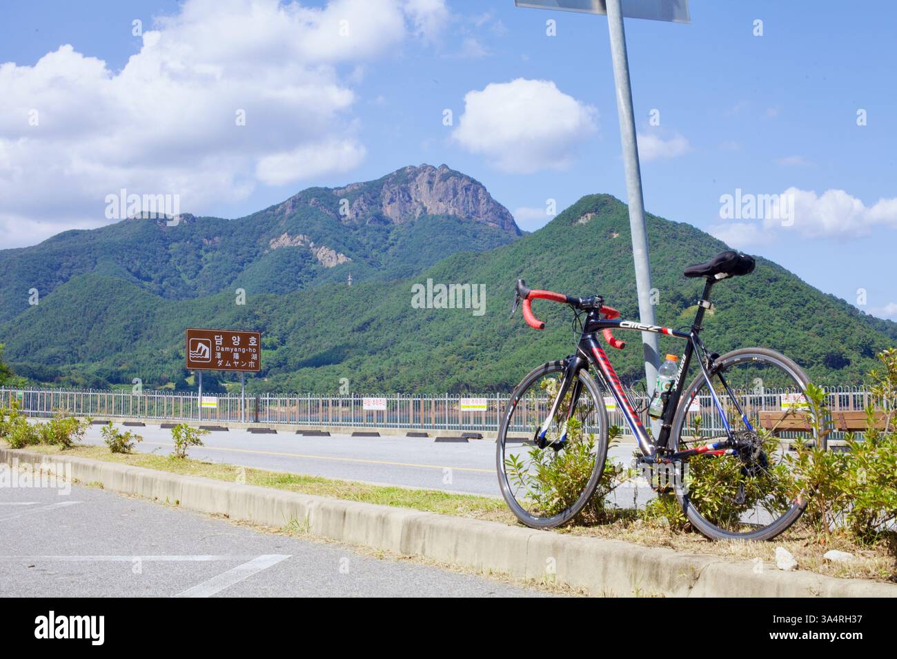 Damyang County, Südkorea - 23. September 2020: Ein Rennrad beugt sich vor einem Wegweiser in der Nähe des Damyang Lake vor der malerischen Kulisse des Jeonggak Mountai Stockfoto