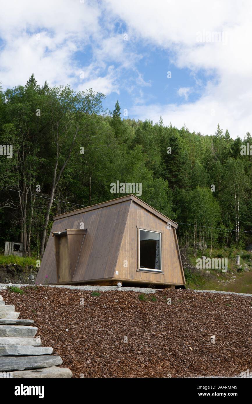 Eine moderne Holzhütte mit eckigem Design befindet sich in einer ruhigen natürlichen Umgebung, umgeben von üppigen grünen Bäumen und einem klaren blauen Himmel, ein umweltfreundliches Hotel Stockfoto