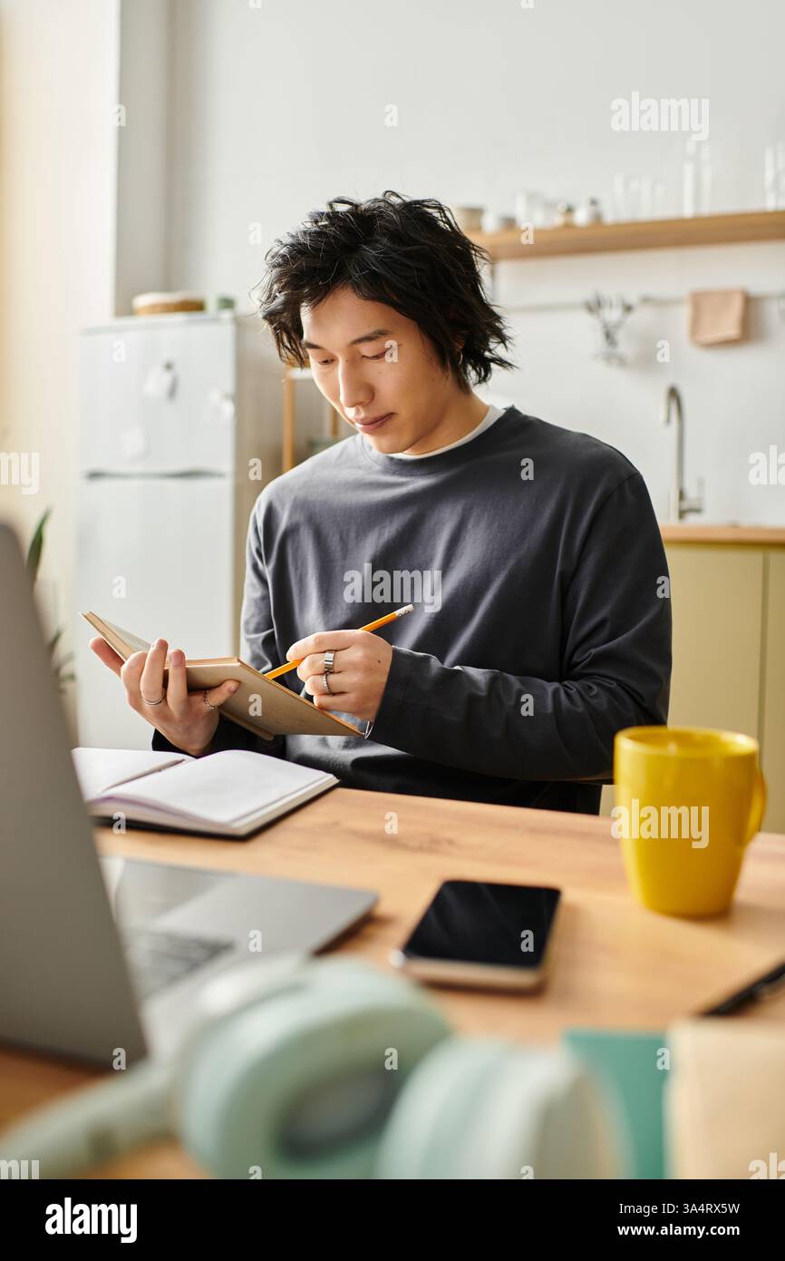 Ein junger asiatischer Mann widmet sich dem Lernen von zu Hause aus, macht Notizen und konzentriert sich auf seine Aufgaben Stockfoto
