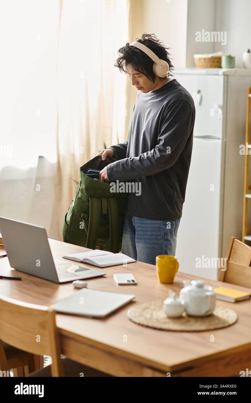 Ein fokussierter junger Mann organisiert seine Lernmaterialien, während er zu Hause online lernen kann. Stockfoto