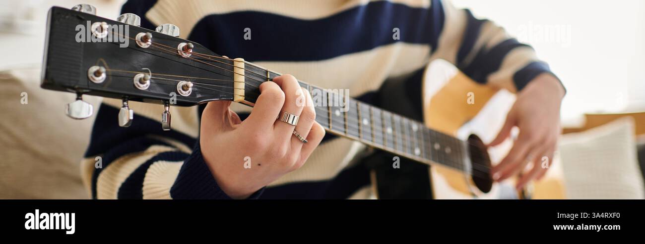 Ein junger Mann übt Akustikgitarre intensiv in einem gemütlichen Raum, Banner Stockfoto