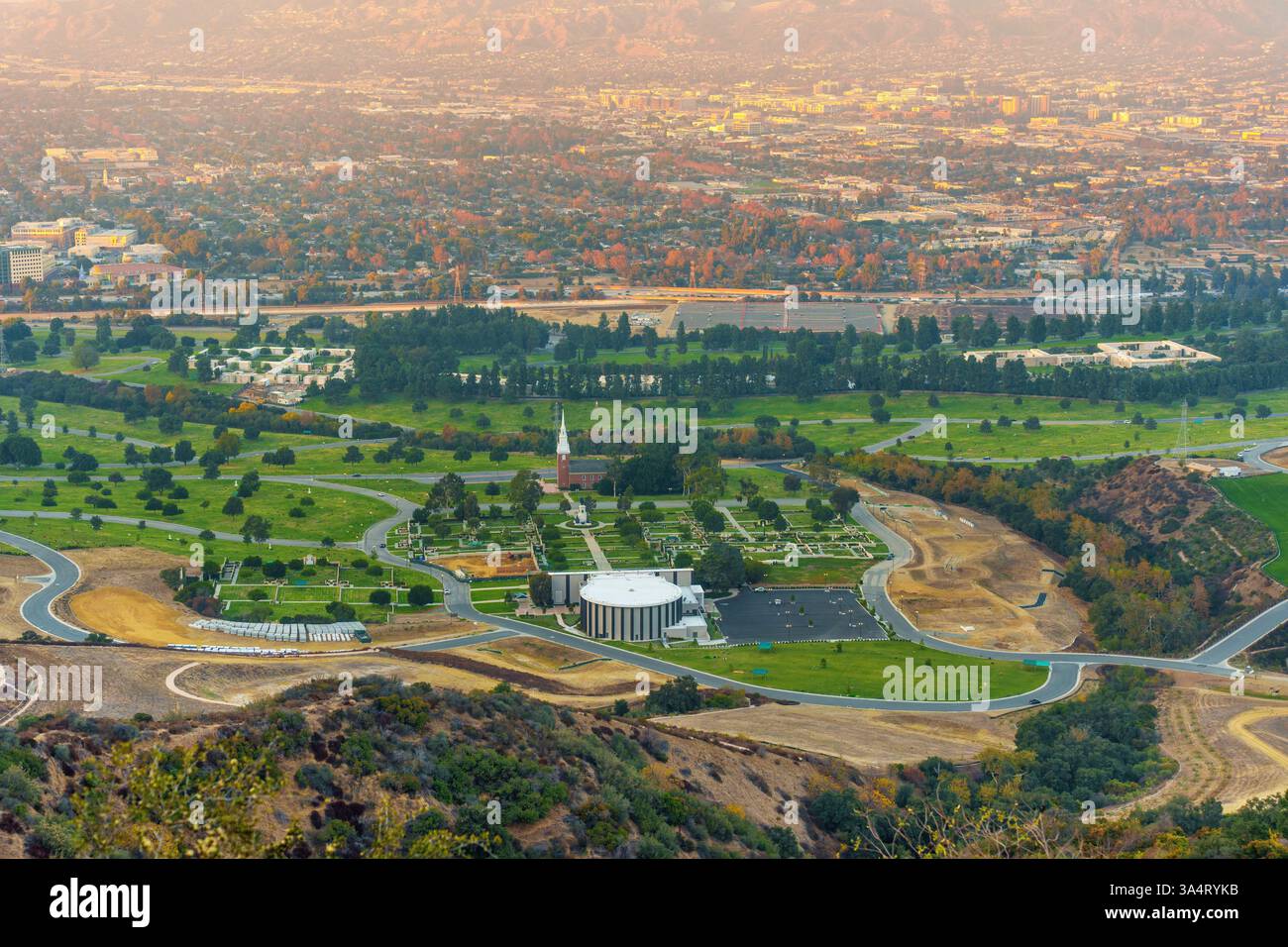 Blick aus der Vogelperspektive auf den Forest Lawn Memorial Park mit üppigem Grün, gepflegten Rasenflächen und bemerkenswerten Strukturen vor einer bergigen Kulisse in Los Angel Stockfoto