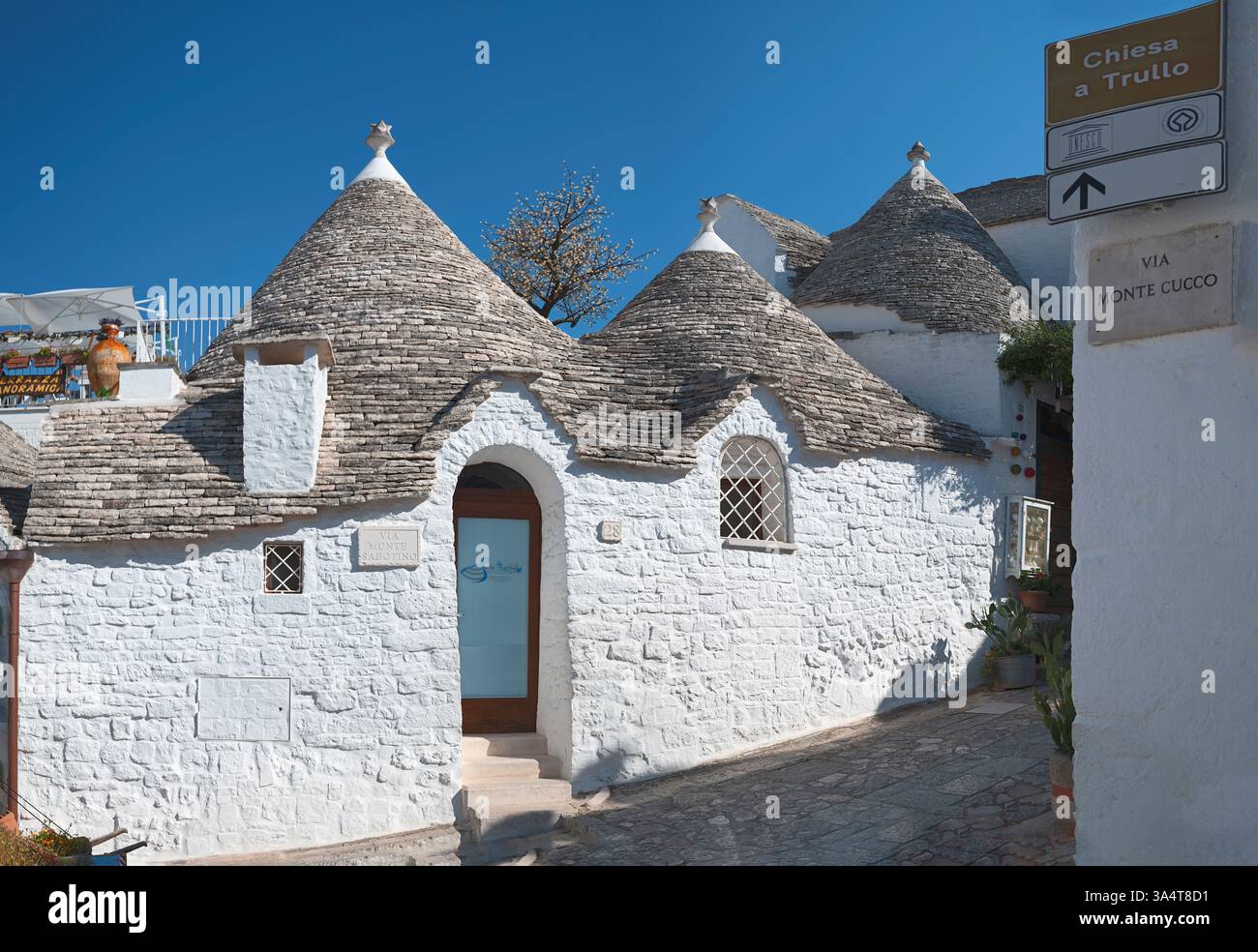 Malerisch von traditionellen Trulli-Häusern in Alberobello, Italien, mit konischen Steindächern. Terrasse mit Panoramablick. Der hellblaue Himmel fügt hinzu Stockfoto