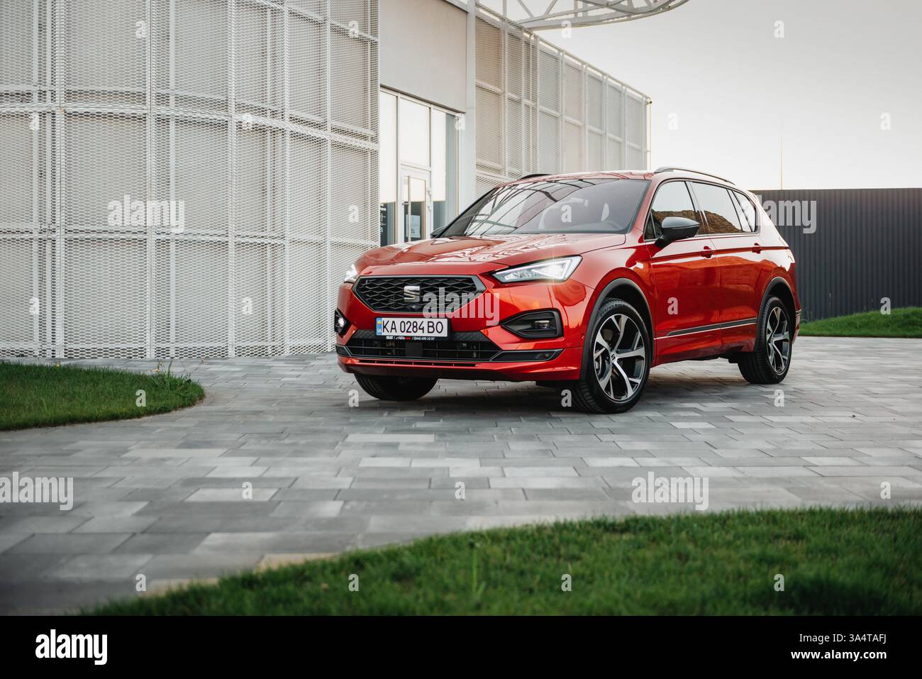 Red SEAT Tarraco parkt in der Nähe des modernen weißen Gebäudes. Vorderansicht des Familien-SUV auf gefliester Einfahrt. Stockfoto