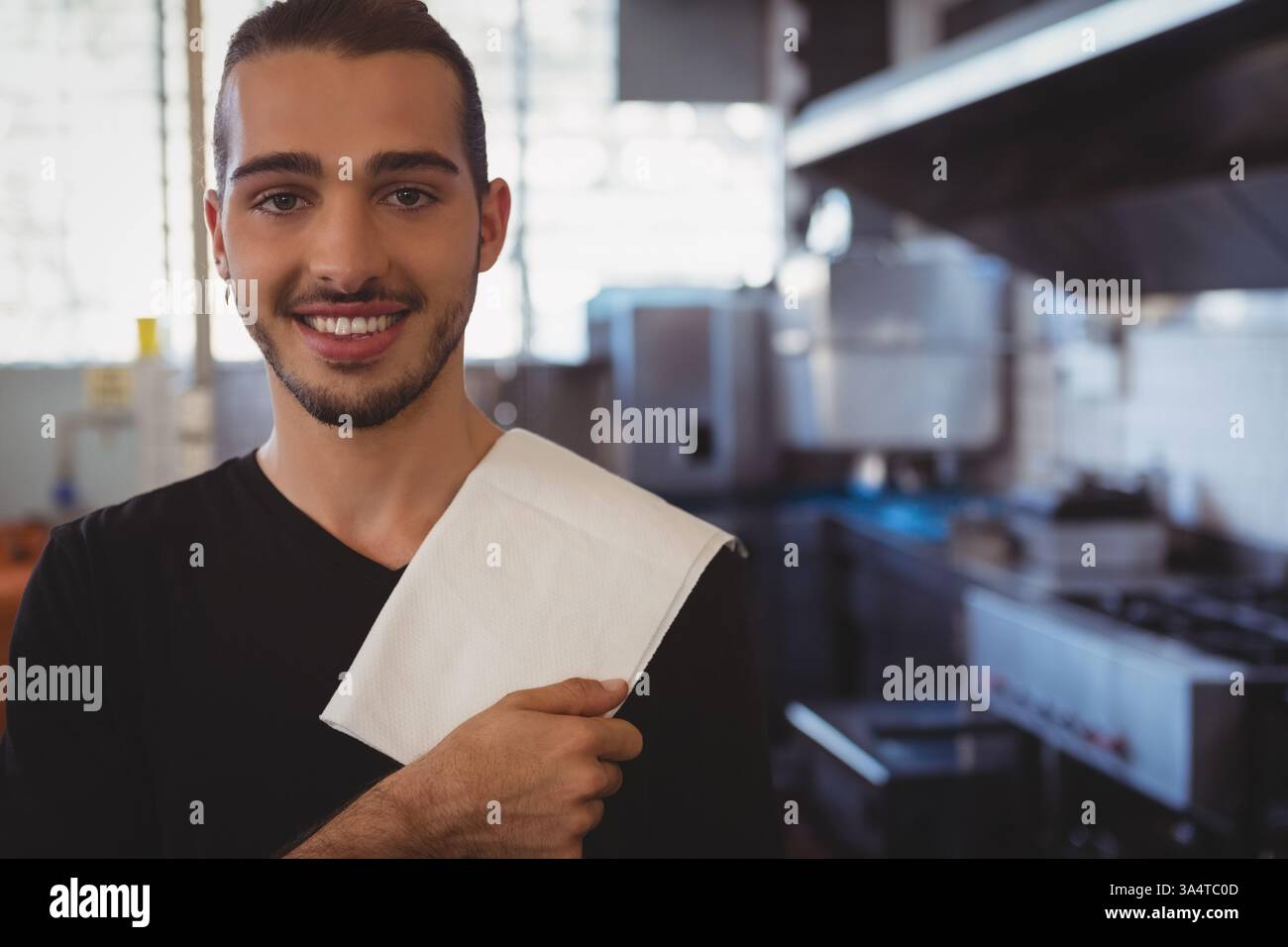Ein lächelnder Barista hält ein Handtuch in der modernen Caféküche, bereit, Gäste zu bedienen, Kopierraum Stockfoto