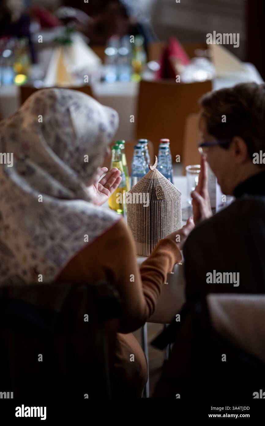 Düsseldorf, Deutschland. März 2025. Zwei Frauen unterhalten sich im Kirchensaal, bevor Christen und Muslime in der Evangelischen Mirjam-Kirche ihr Fasten brechen. In diesem Jahr überschneiden sich die Fastenzeiten von Muslimen und Christen. Die Kampagne soll Ähnlichkeiten hervorheben und das Verständnis fördern. Quelle: Fabian Strauch/dpa/Alamy Live News Stockfoto