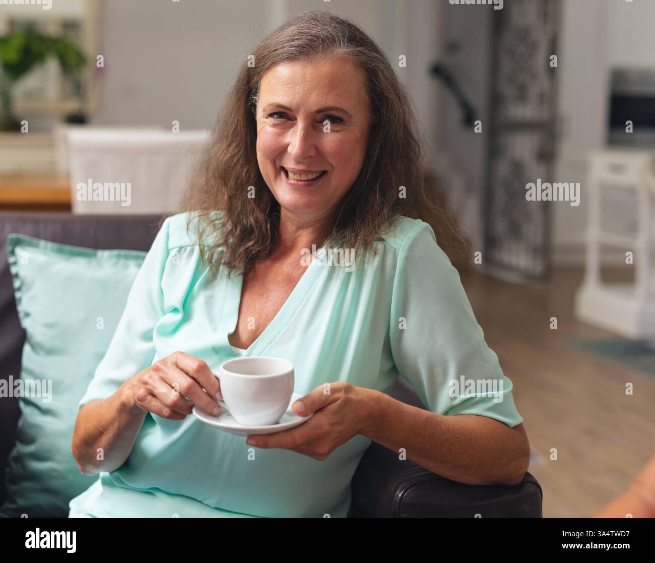 Lächelnde Frau, die zu Hause Kaffee genießt, sich auf einem bequemen Sofa entspannt Stockfoto