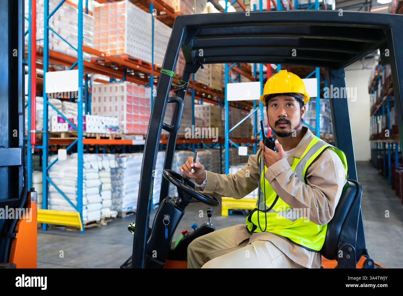 Lagerarbeiter in Sicherheitsausrüstung, der Gabelstapler bedient und über Funk, Kopierraum kommuniziert Stockfoto