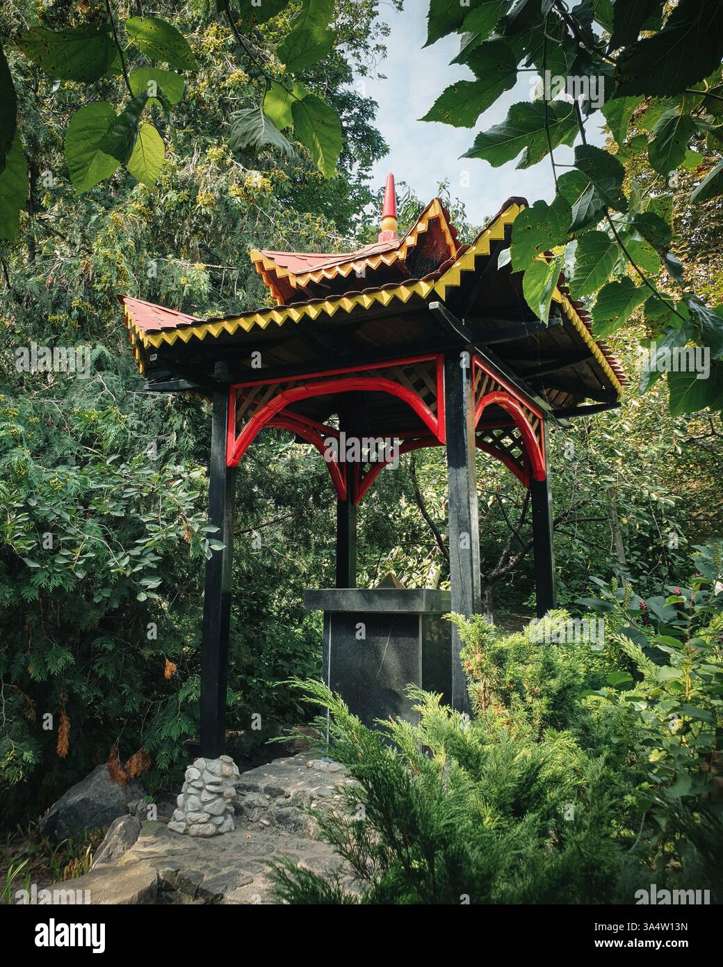 Kleiner buddhistischer Pavillon in einem Garten. Hölzerner Pavillon umgeben von grünen Sträuchern. Stockfoto