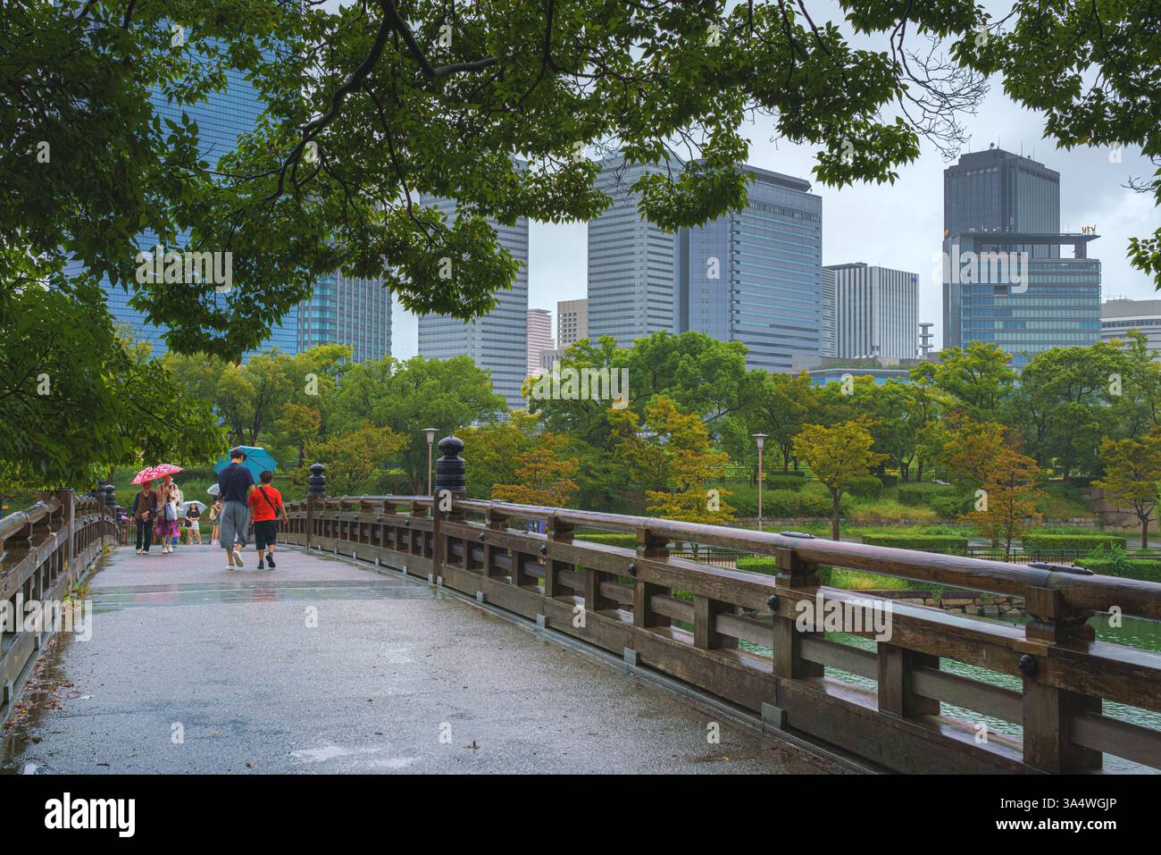 Osaka, Japan - 22. September 2024, Panoramablick durch das Laub der Bäume zu den Wolkenkratzern und die Brücke über den Graben mit Menschen, vor O Stockfoto