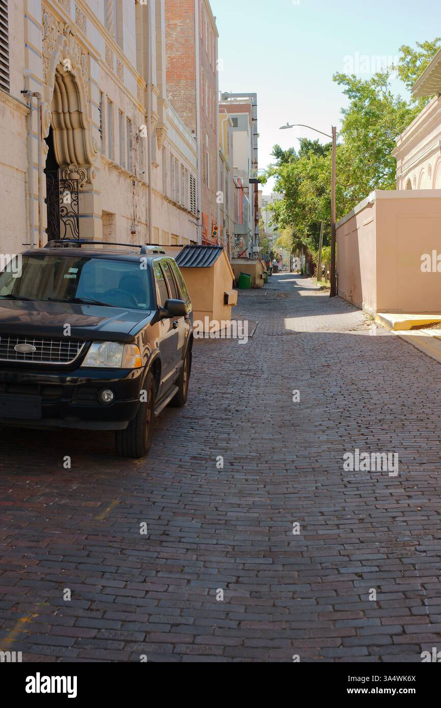 SUV parkte auf einer Backsteinstraße in einer Gasse. Das Fahrzeug befindet sich auf der linken Seite. Die Gasse ist eng und mit rötlich-braunen Ziegeln gepflastert, die Zeichen von zeigen Stockfoto