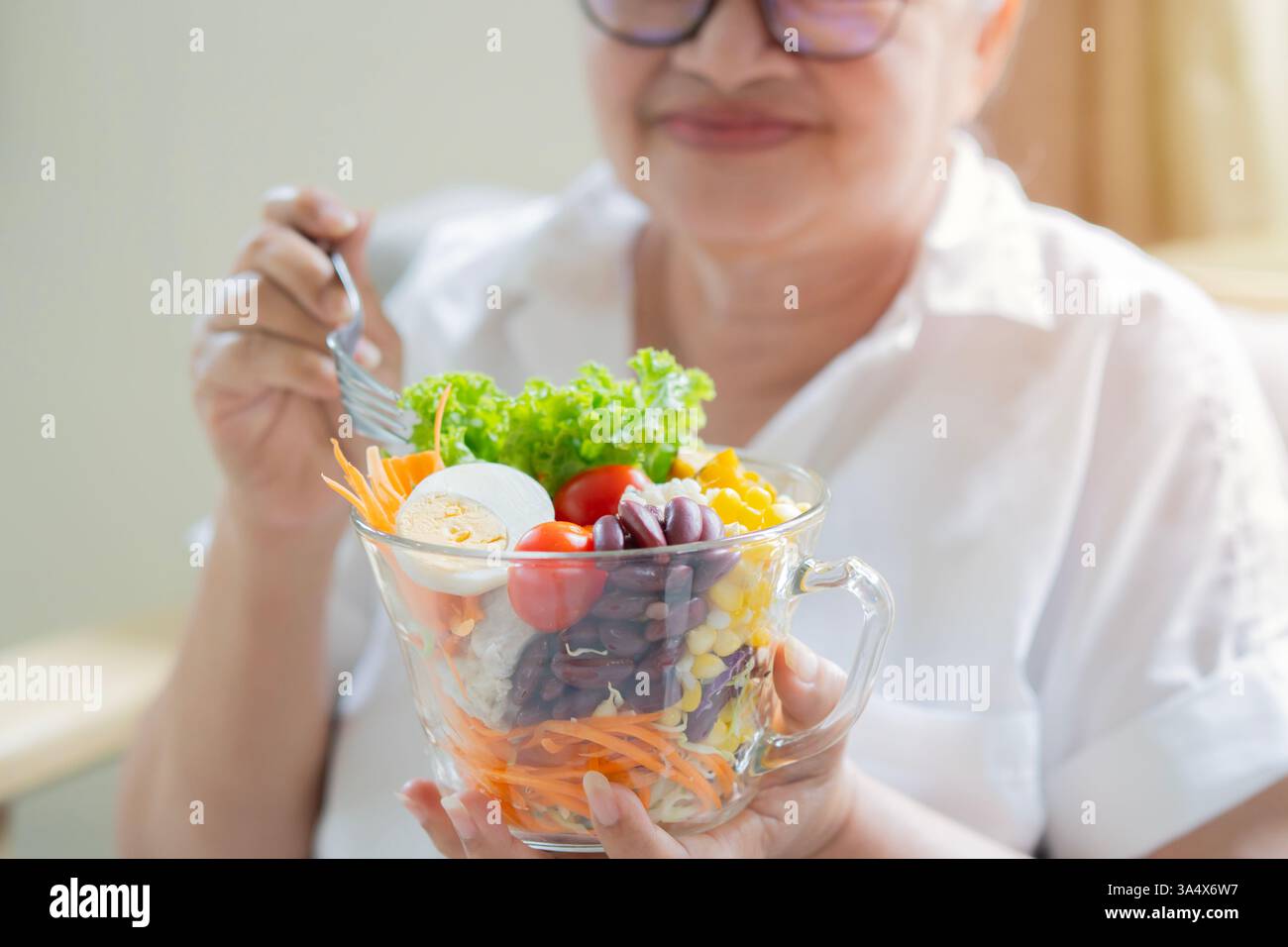 Eine ältere Frau, die bereit ist, einen Salat aus frischen und getrockneten Früchten zu essen. Frühstück oder Mittagessen, Konzept für gesunde Ernährung. Stockfoto