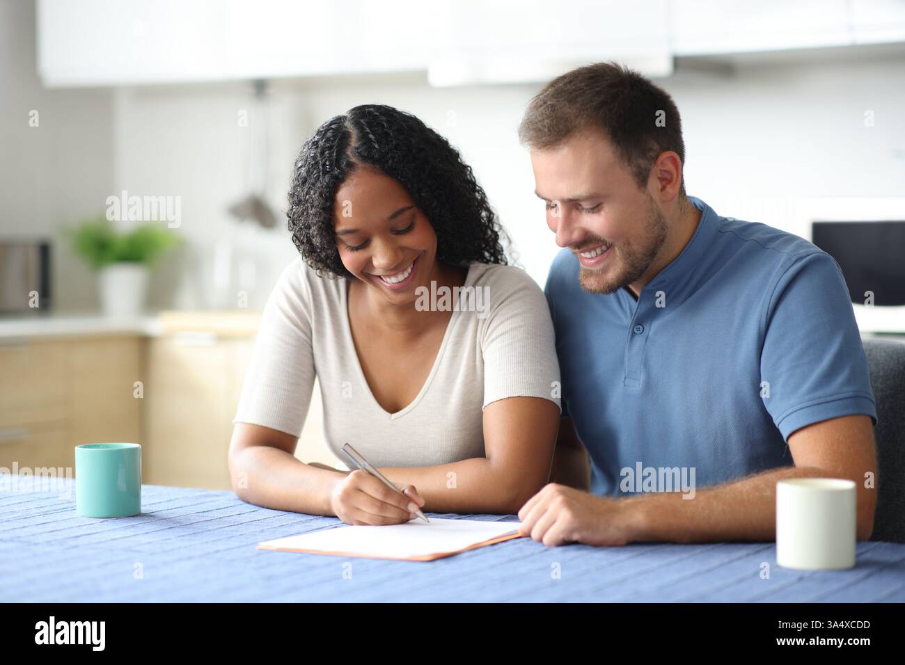 Glückliches interrassisches Paar, das Papiervertrag in der Küche zu Hause unterzeichnet Stockfoto