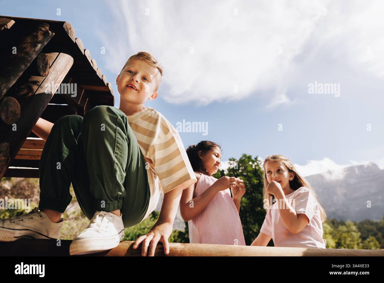 Drei Kinder haben Spaß auf einem Spielplatz im Freien, umgeben von Natur und Sonne. Die Szene fängt die Unschuld und Freude der Kindheit in einem Hauch ein Stockfoto