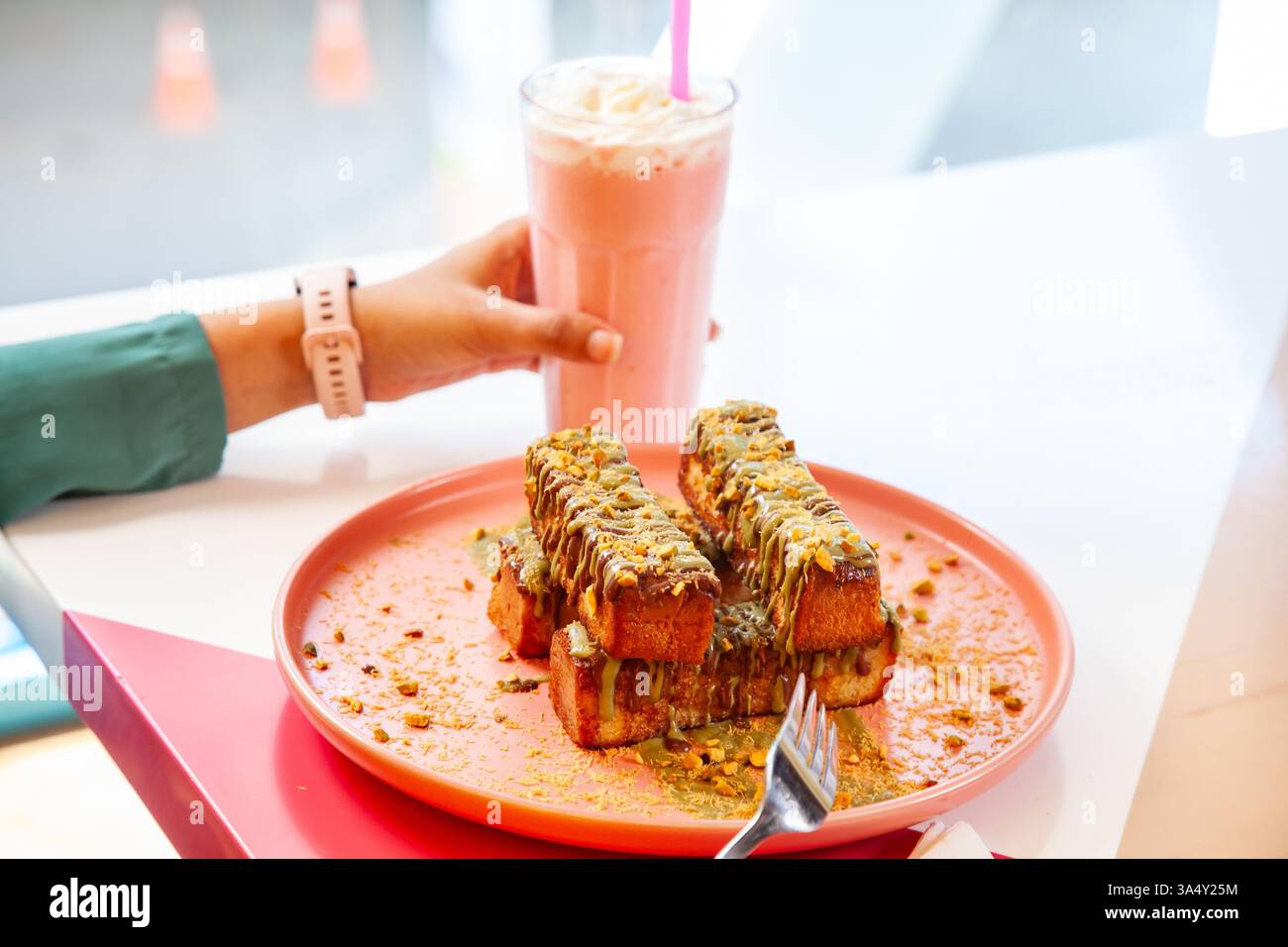 französischer Zimt-Toast mit Pistazienbelag, serviert mit Milchshake in einem schicken Café-Restaurant. Stockfoto