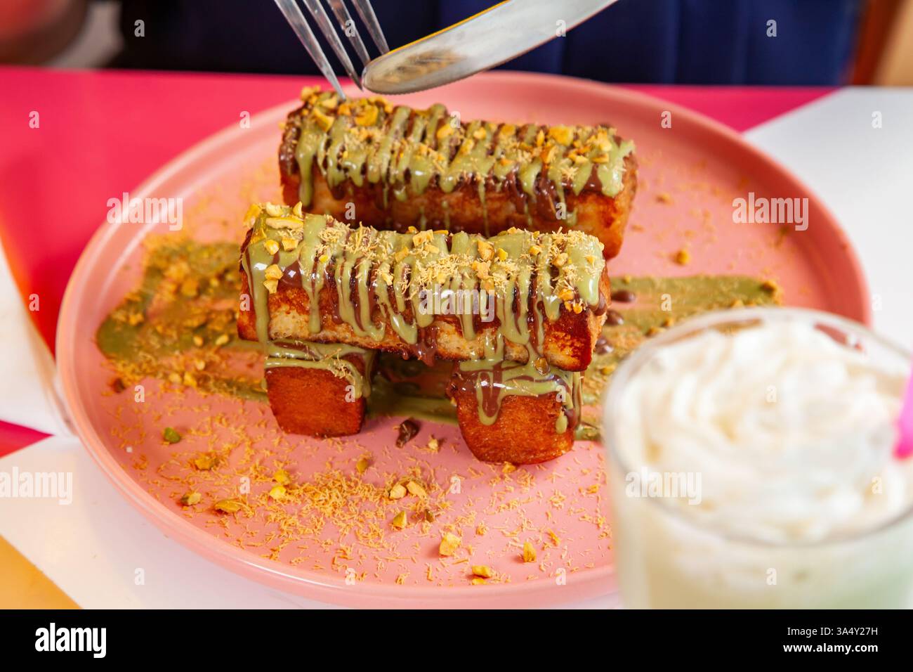 französischer Zimt-Toast mit Pistazienbelag, serviert mit Milchshake in einem schicken Café-Restaurant. Stockfoto