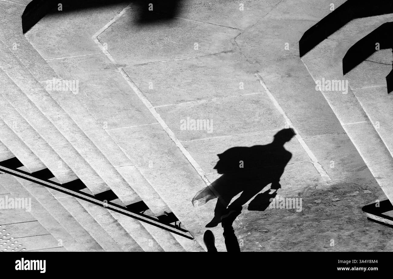 Schattensilhouette einer Person, die auf dem Stadtplatz läuft, in Schwarz-weiß Stockfoto