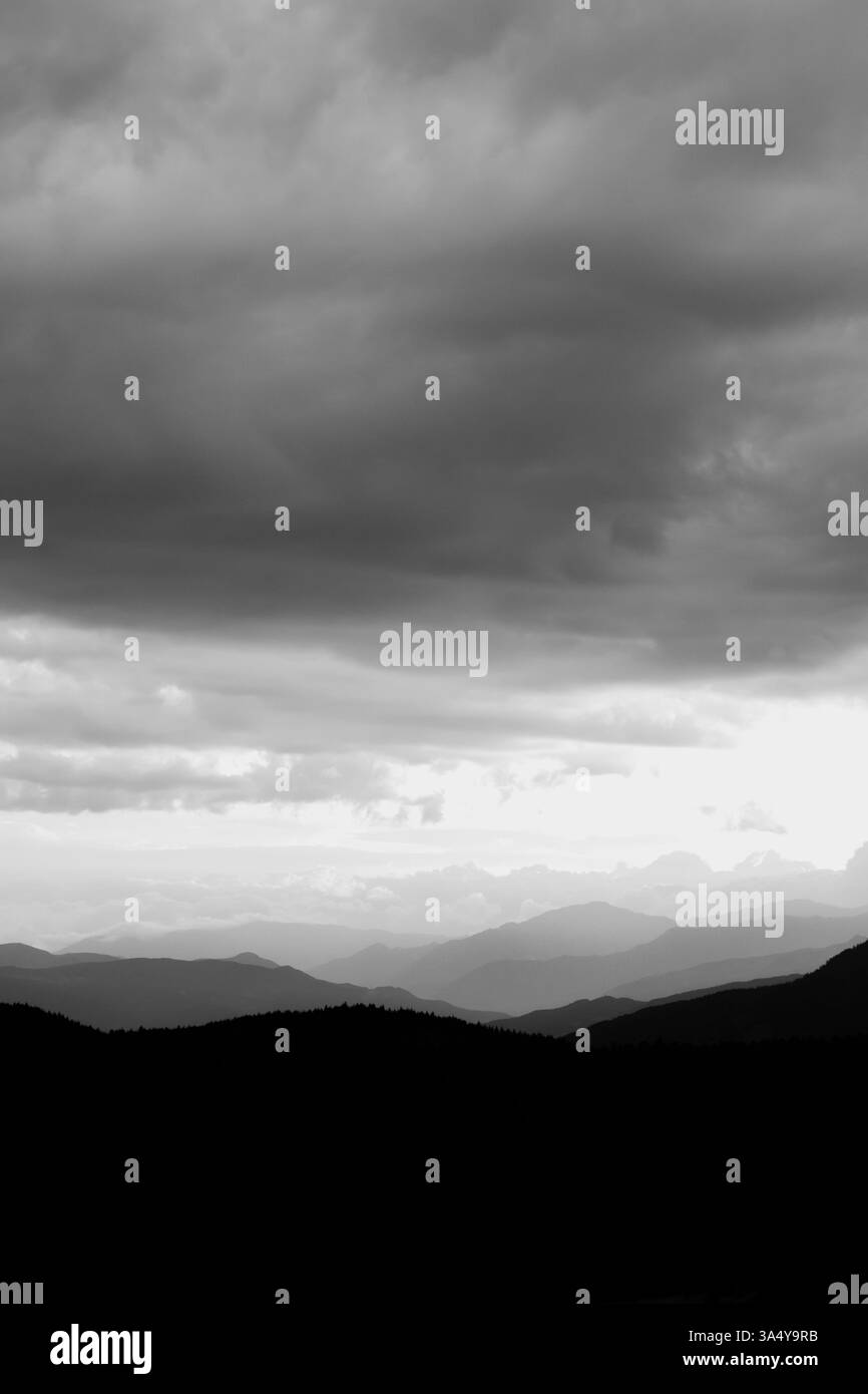 Überlagerte Berge und bewölkter Himmel. Vertikales Schwarzweiß-Foto im Querformat. Stockfoto