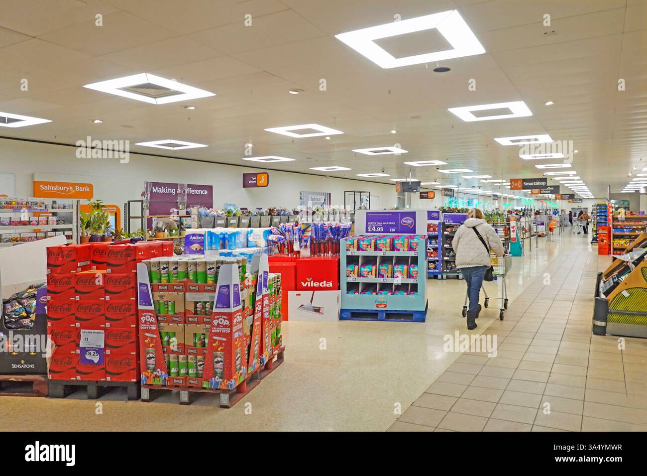 Rückansicht einer Käuferin, die einen Supermarktwagen in Richtung grünes Licht schiebt, an der Kasse Innenansicht der Kassen im Sainsburys-Geschäft Essex England Großbritannien Stockfoto