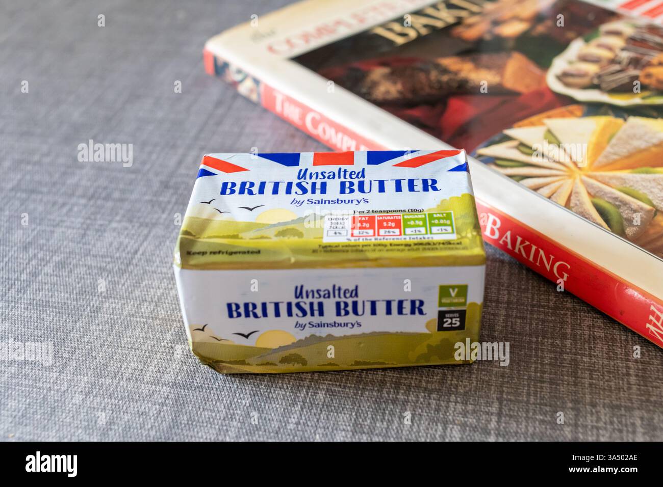 Gewickelter ungesalzener Butterblock von Sainsburys mit einem Backbuch im Hintergrund Stockfoto