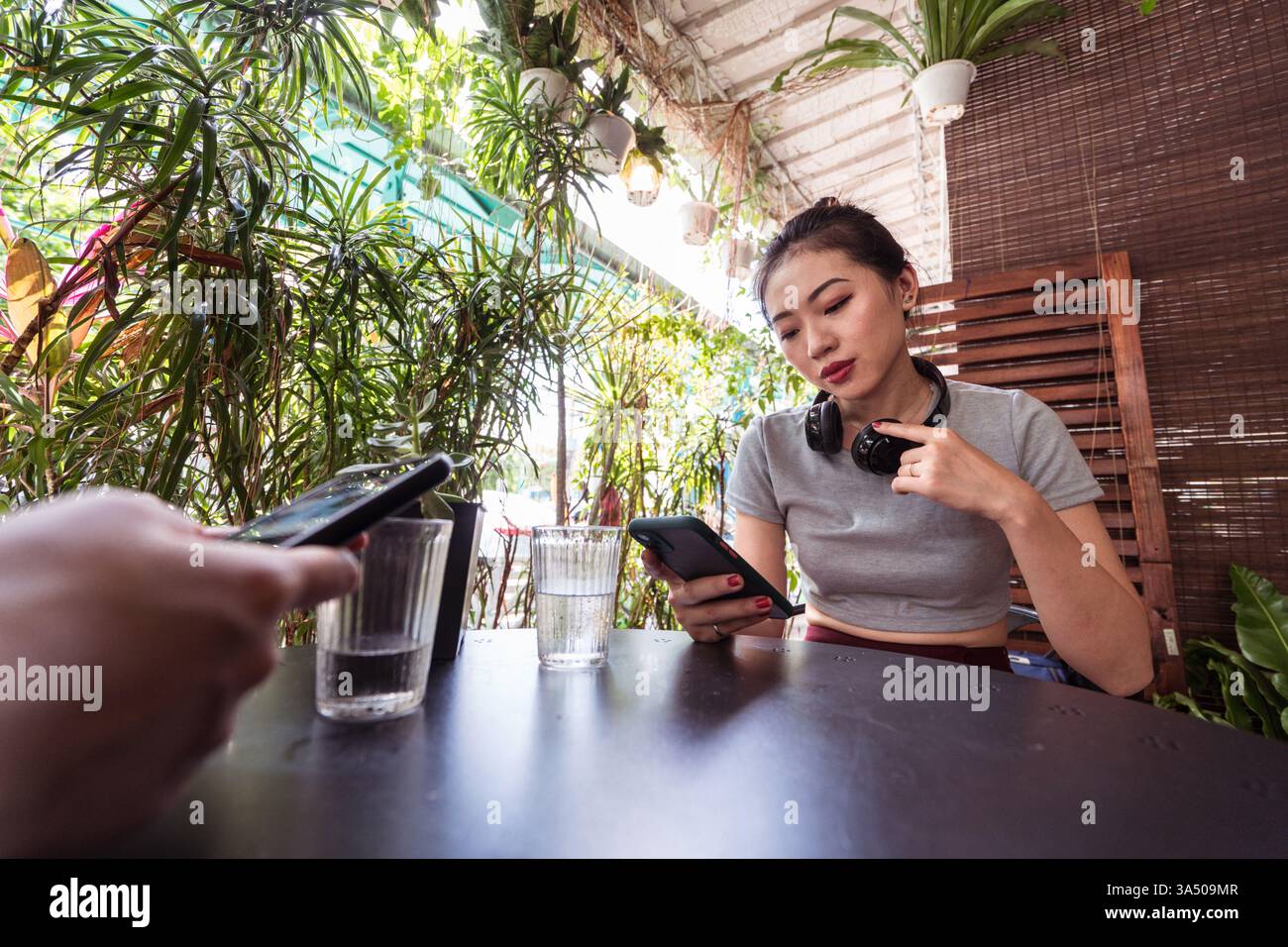Asiatische Frauen, die in einem Café Smartphones surfen. Ein lässiges, modernes Lifestyle-Image, das perfekt für Geschichten über soziale Medien, Konnektivität und mobiles Surfen geeignet ist. Ideal für Apps, digitale Dienste und Kampagnen zur Kaffeekultur. Stockfoto