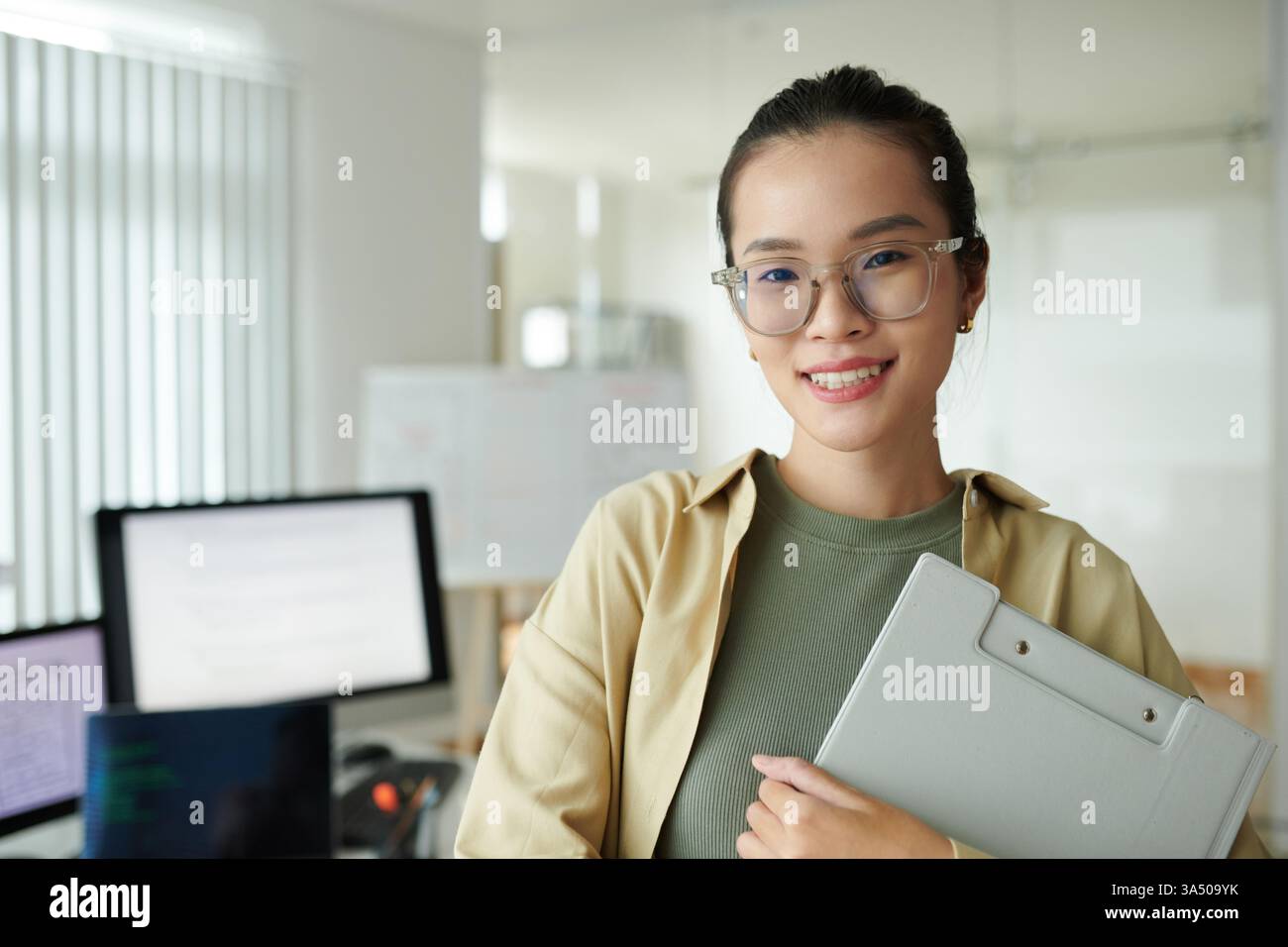 Porträt einer fröhlichen jungen Software-Entwicklerin, die an ihrem neuen Arbeitsplatz steht. Das Image vermittelt Selbstvertrauen und Begeisterung in einer technischen Karriere, die sich für IT, Softwareentwicklung und weibliche Empowerment-Themen eignet. Ideal für Technologiemarken und Rekrutierungskampagnen. Stockfoto