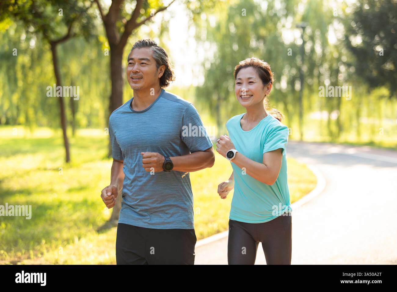 Lächelndes chinesisches Paar mittleren Alters, das tagsüber zusammen im Park läuft Stockfoto