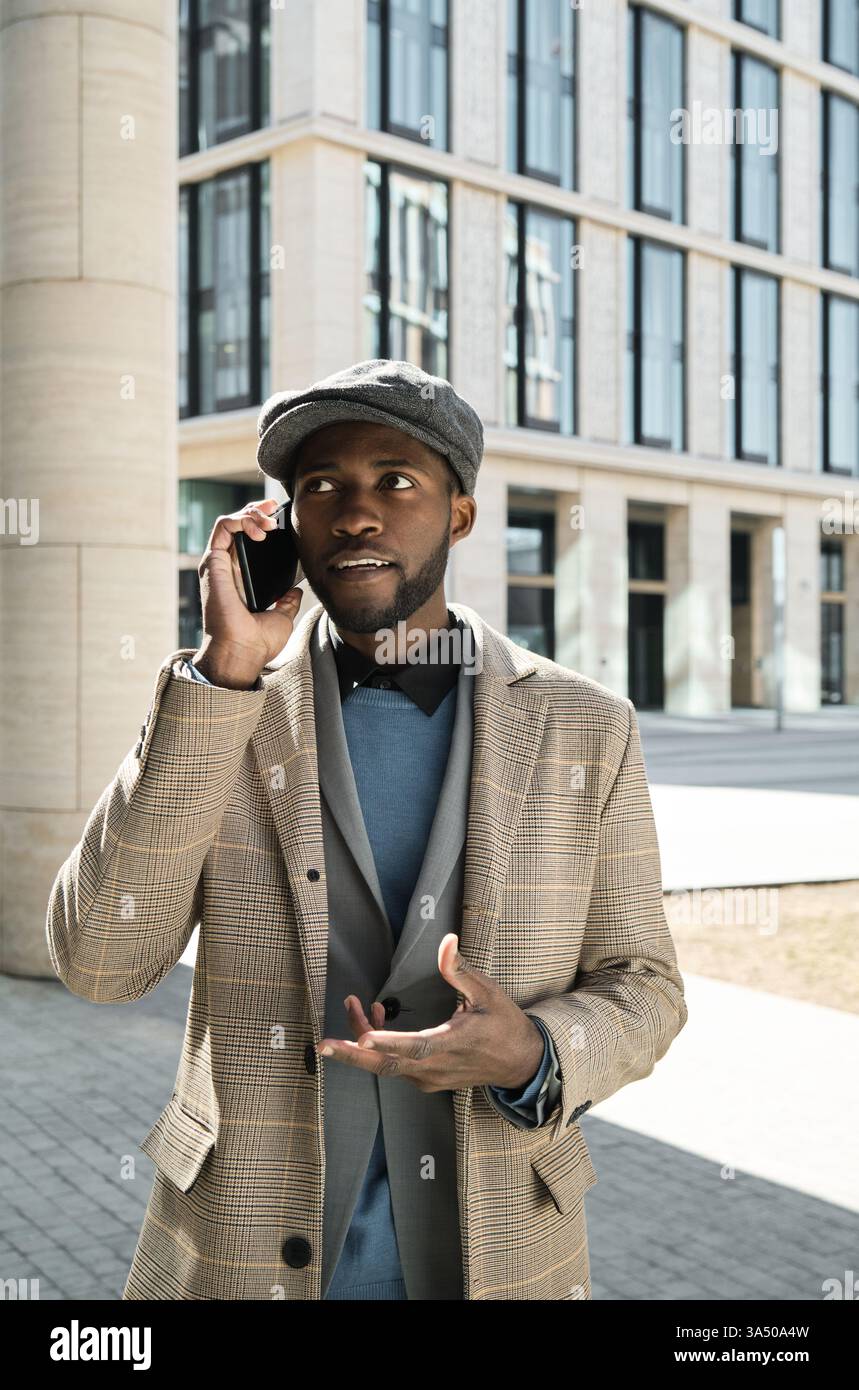 Junger afrikanischer Geschäftsmann, der mit einem Handy in einer städtischen Umgebung spricht. Ein selbstbewusstes, modernes professionelles Image für Geschäfts- und Netzwerkkontexte. Stockfoto