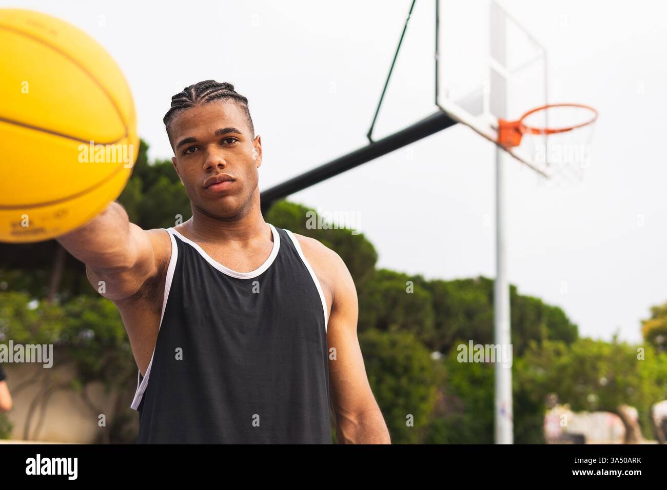 Hispanischer Mann hält tagsüber einen Basketball neben dem Basketball in einem Park. Ein energiegeladenes Bild für Sport und Outdoor-Aktivitäten, das sich für Fitness, Basketball-Kampagnen und das Erzählen von Geschichten aus dem Jugendsport eignet. Ideal für aktive Lifestyle-Aktionen. Stockfoto