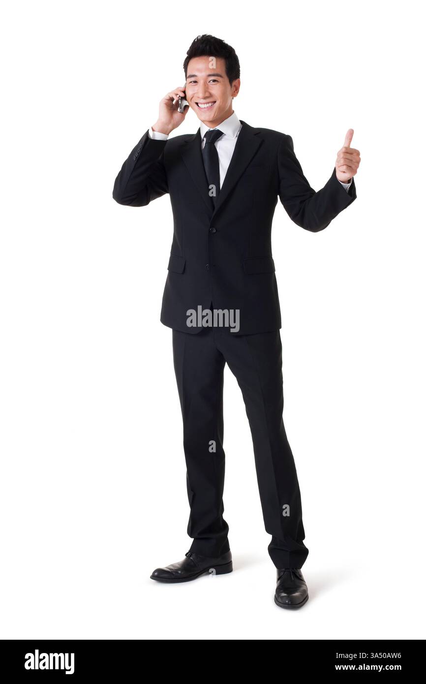 Fröhlicher chinesischer Geschäftsmann, der einen Daumen hoch hält, vor einem sauberen weißen Studio-Hintergrund. Ideal für Kommunikation, Erfolg und positive Geschäftsnachrichten. Stockfoto
