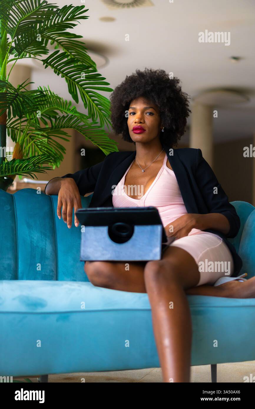 Die junge schwarze Unternehmerin führt während eines Arbeitstreffens einen Videoanruf in einem rosa Kleid und einer schwarzen Jacke. Spiegelt Telearbeit und virtuelle Zusammenarbeit in einem modernen Geschäftsumfeld wider. Geeignet für Geschichten über Startups, Remote-Teams und Online-Meetings. Stockfoto