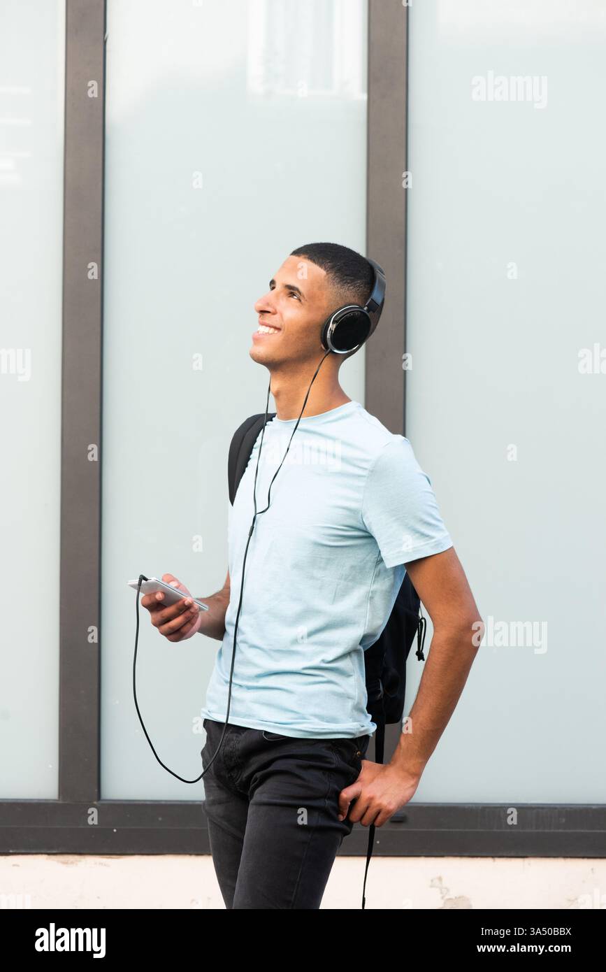 Arabischer Mann, der draußen mit Kopfhörern Musik hört, aufblickt. Lässiges Lifestyle-Porträt für Jugendliche, Musik und Outdoor-Momente. Stockfoto