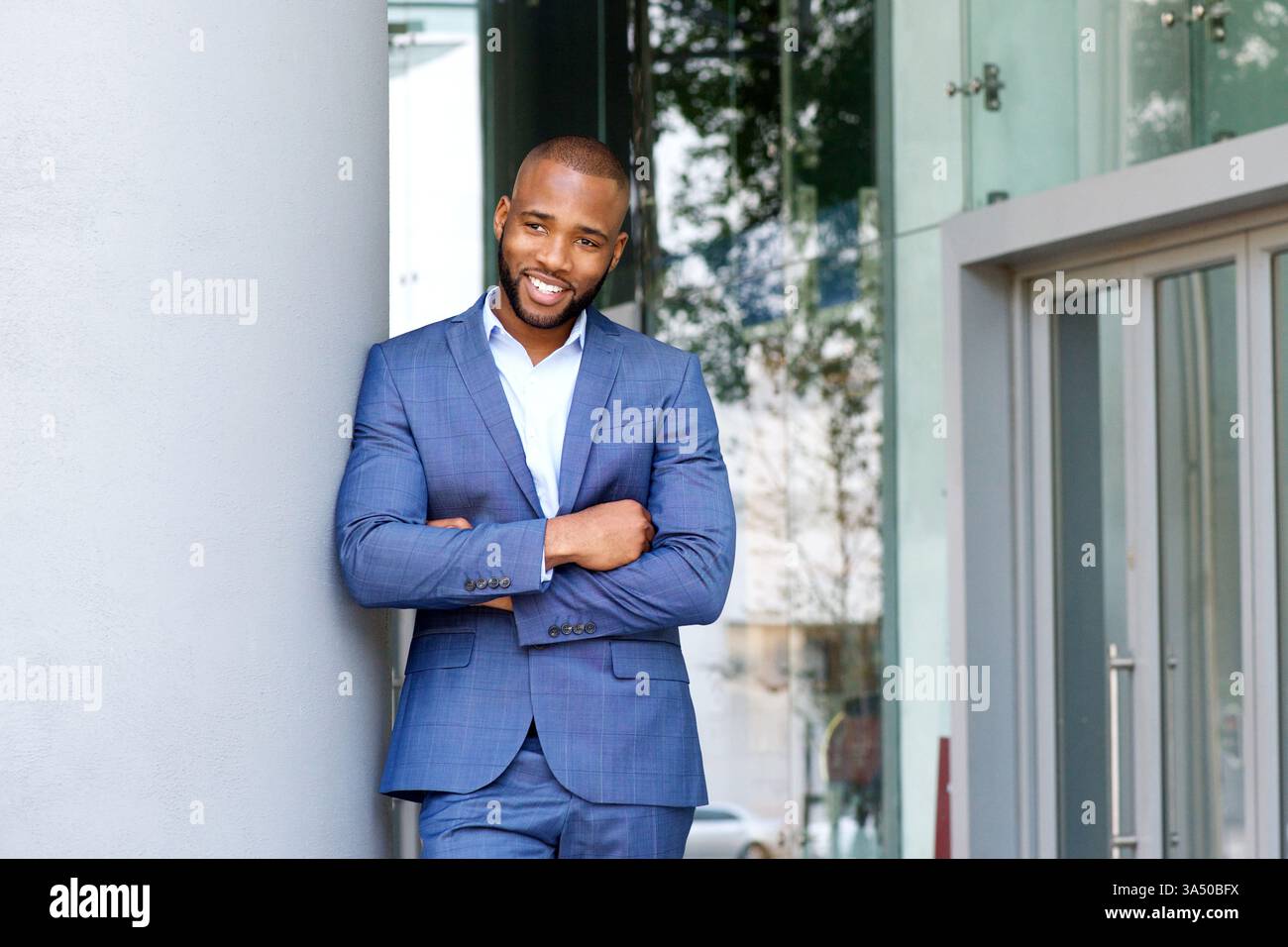 Porträt eines lächelnden Geschäftsmannes draußen, der sich an eine Wand lehnt. Diese moderne Führungskraft strahlt Vertrauen in eine urbane Umgebung aus und ist somit ideal für Unternehmensprofile und Kampagnen zum Geschäftsleben. Ein vielseitiges Image für Präsentationen, Marketing und professionelle Kommunikation. Stockfoto