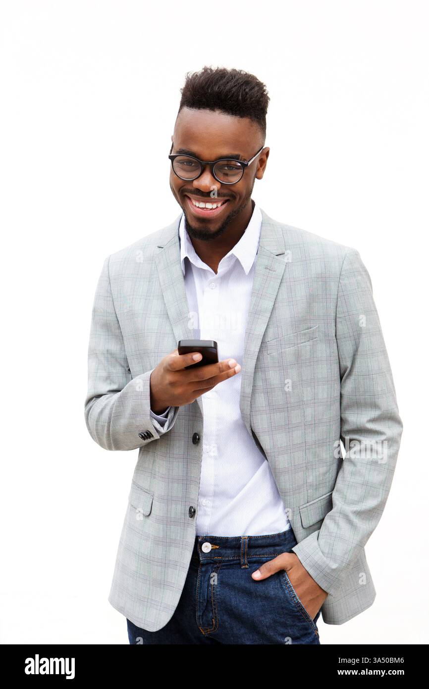Der lächelnde Schwarze Mann steht vor einem weißen Hintergrund und hält ein Smartphone mit einer Hand in der Tasche. Dieses moderne Porträt bietet einen sauberen Kopierraum für Branding oder Text. Stockfoto