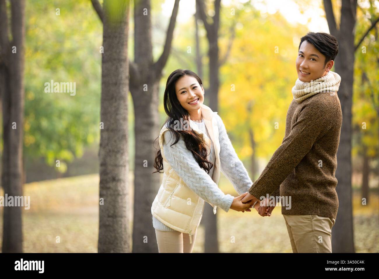 Ein lächelndes chinesisches Paar hält Hände, während er im Herbst im Park steht Stockfoto