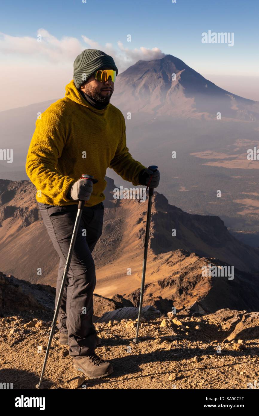 Entschlossene Wanderer wandern auf zerklüfteten Pfaden von Iztaccihuatl mit einem entfernten Vulkan, der bei Sonnenaufgang am Horizont aufsteigt. Diese Outdoor-Abenteuerszene zeigt Berglandschaften, Trekkingausrüstung und den Geist der Erkundung. Stockfoto